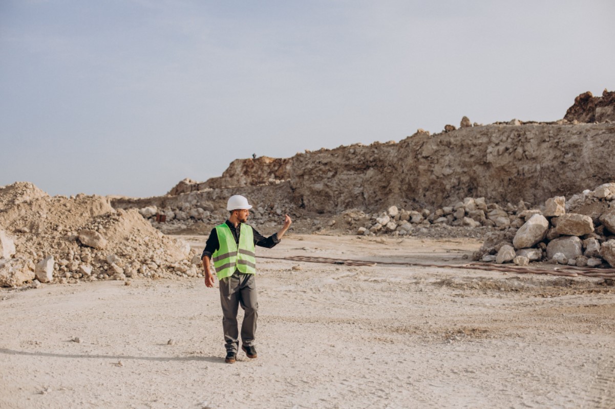An archaeologist wearing a hi-vis vest and white hard hat works at a site