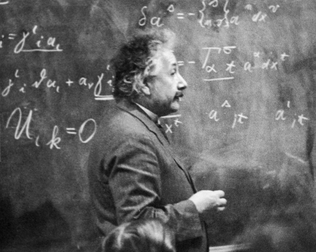 Physicist Albert Einstein teaching in front of a chalkboard filled with mathematical calculations