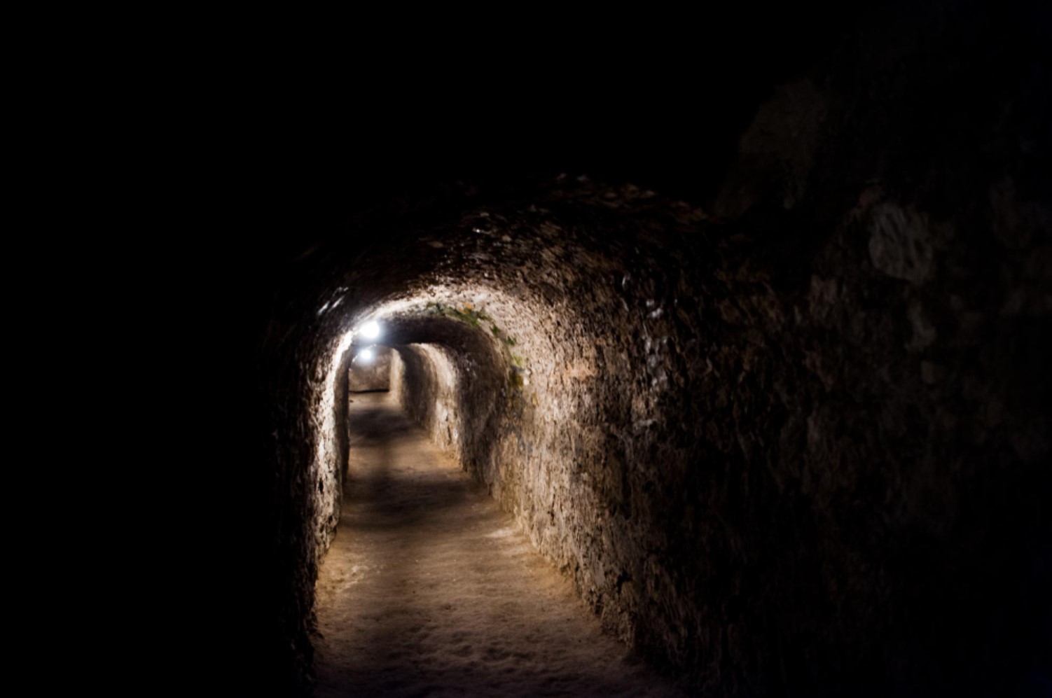 Dark passageway, which is part of a tunnel system, is lit up by a single light