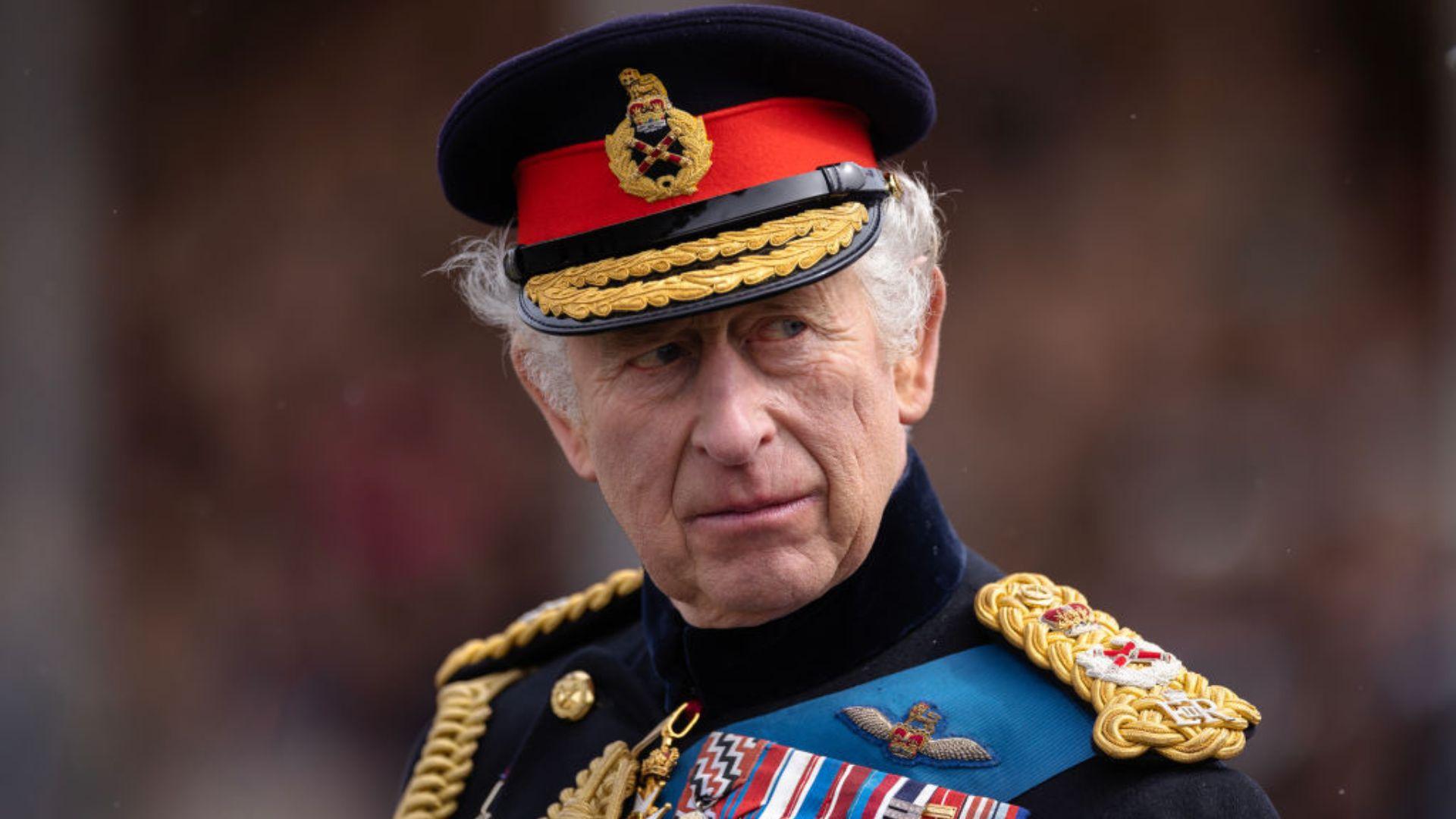 Close-up portrait of King Charles III wearing a red military beret with a badge and a navy blue uniform adorned with various medals