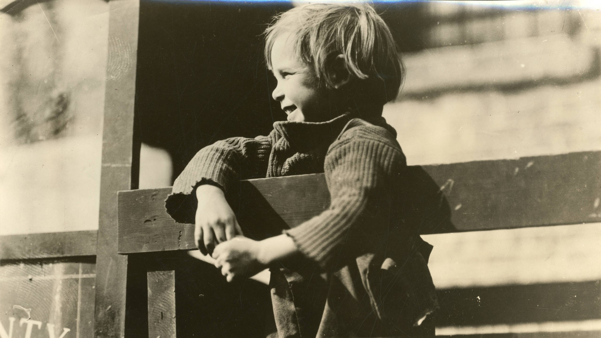 Jackie Coogan hanging onto a fence and smiling in the film The Kid.