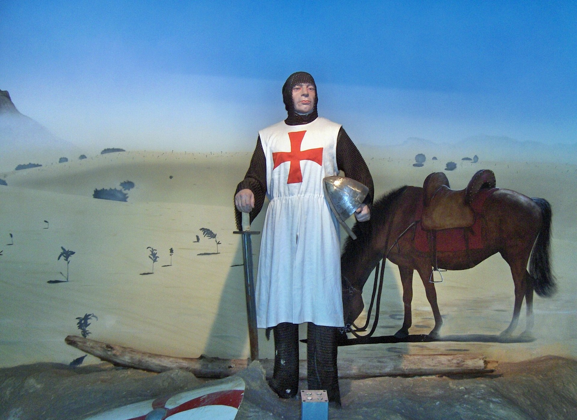 A life-like statue wearing a white cloak with a red cross while holding a sword