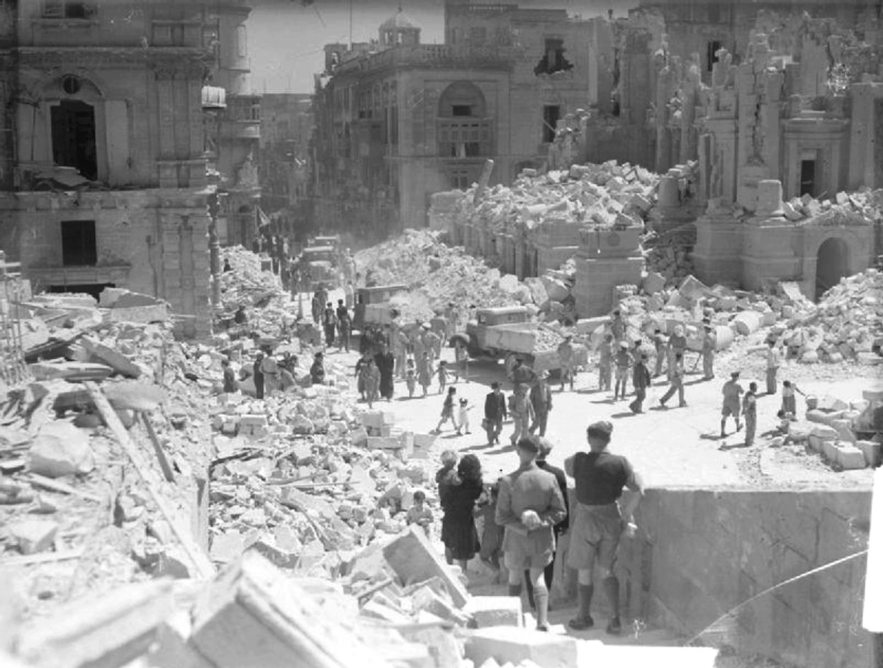 Civilians and service personnel try to clean the rumble of a heavily bomb-damaged street in Valletta, Malta