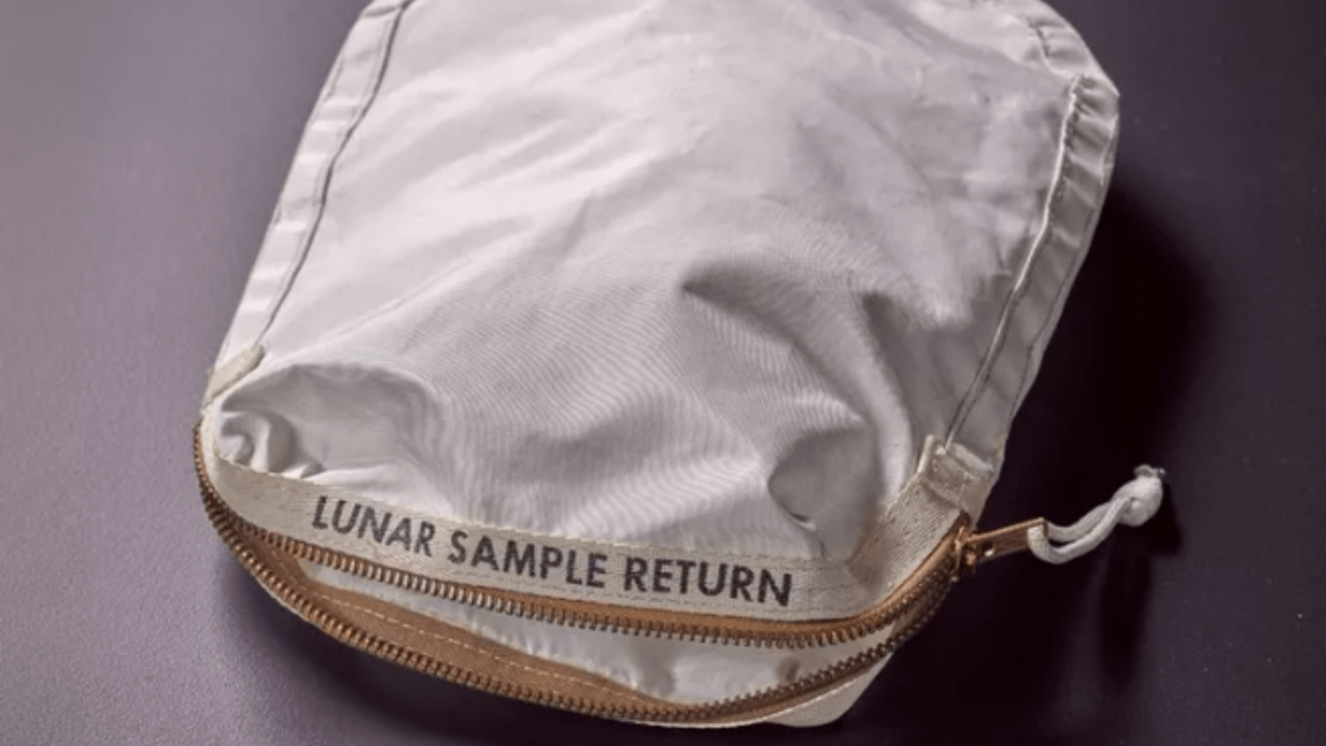 A white bag with a gold zipper that has “lunar sample return” written on it in black block letter near the zipper’s opening.
