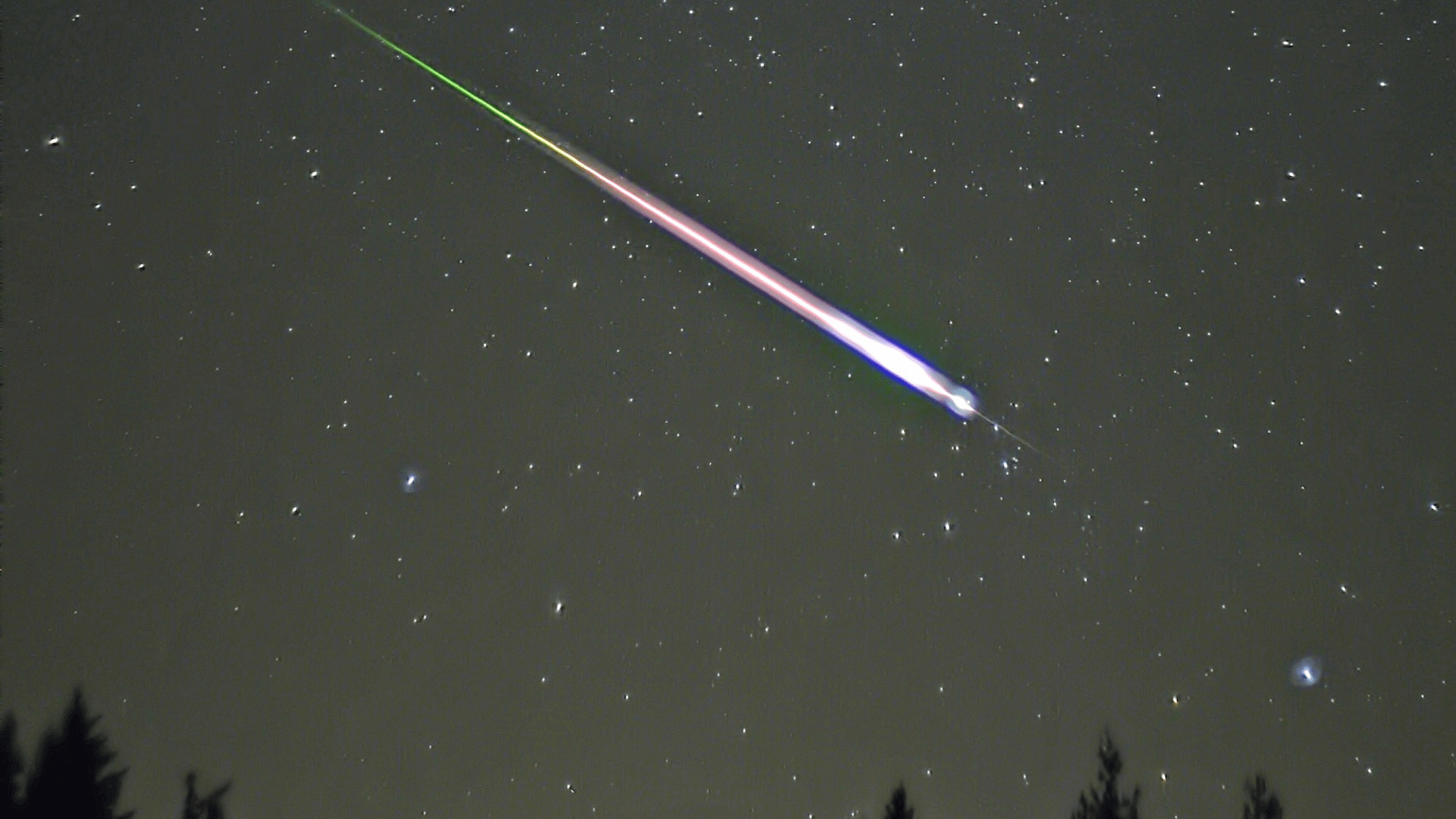 A meteor streaking through the night sky, leaving a purple trail of light that fades to green.