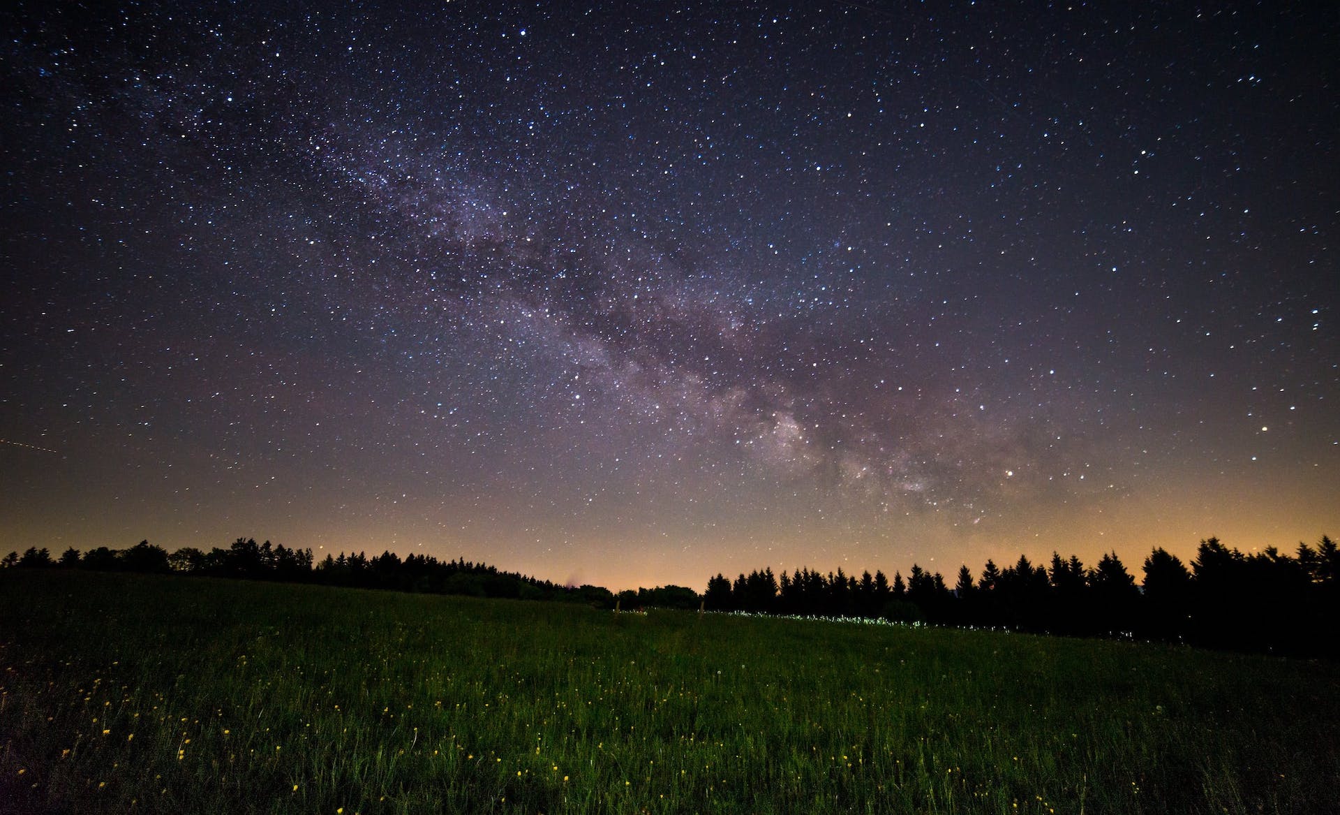 The galaxy over an open field and a tree line