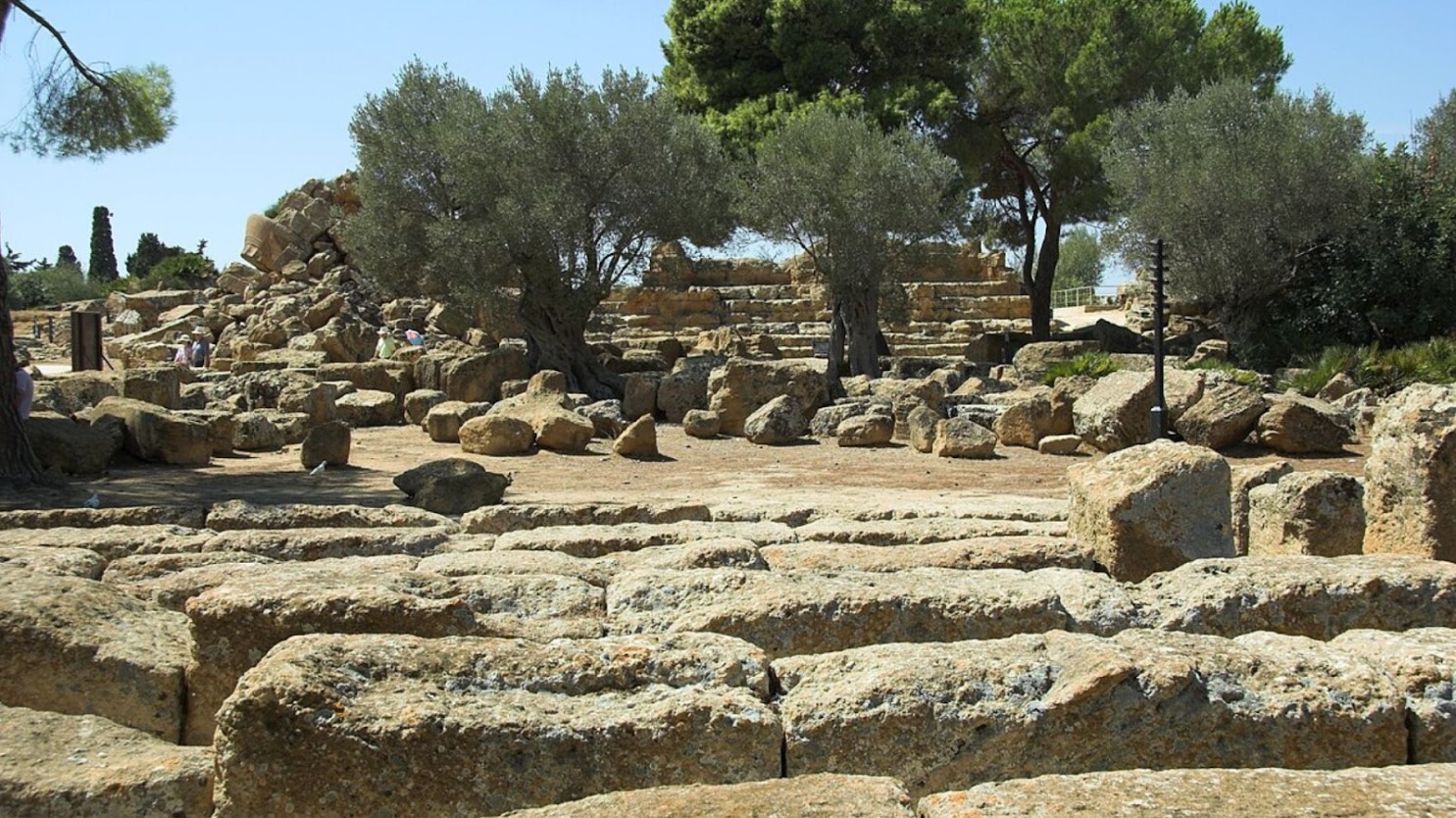 Greek ruins of a temple with green trees interspersed amongst the stones.