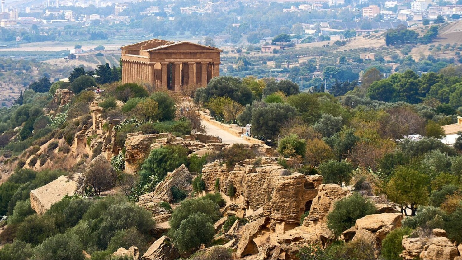 Ruins of a temple sit proudly on a hill overlooking a modern town.