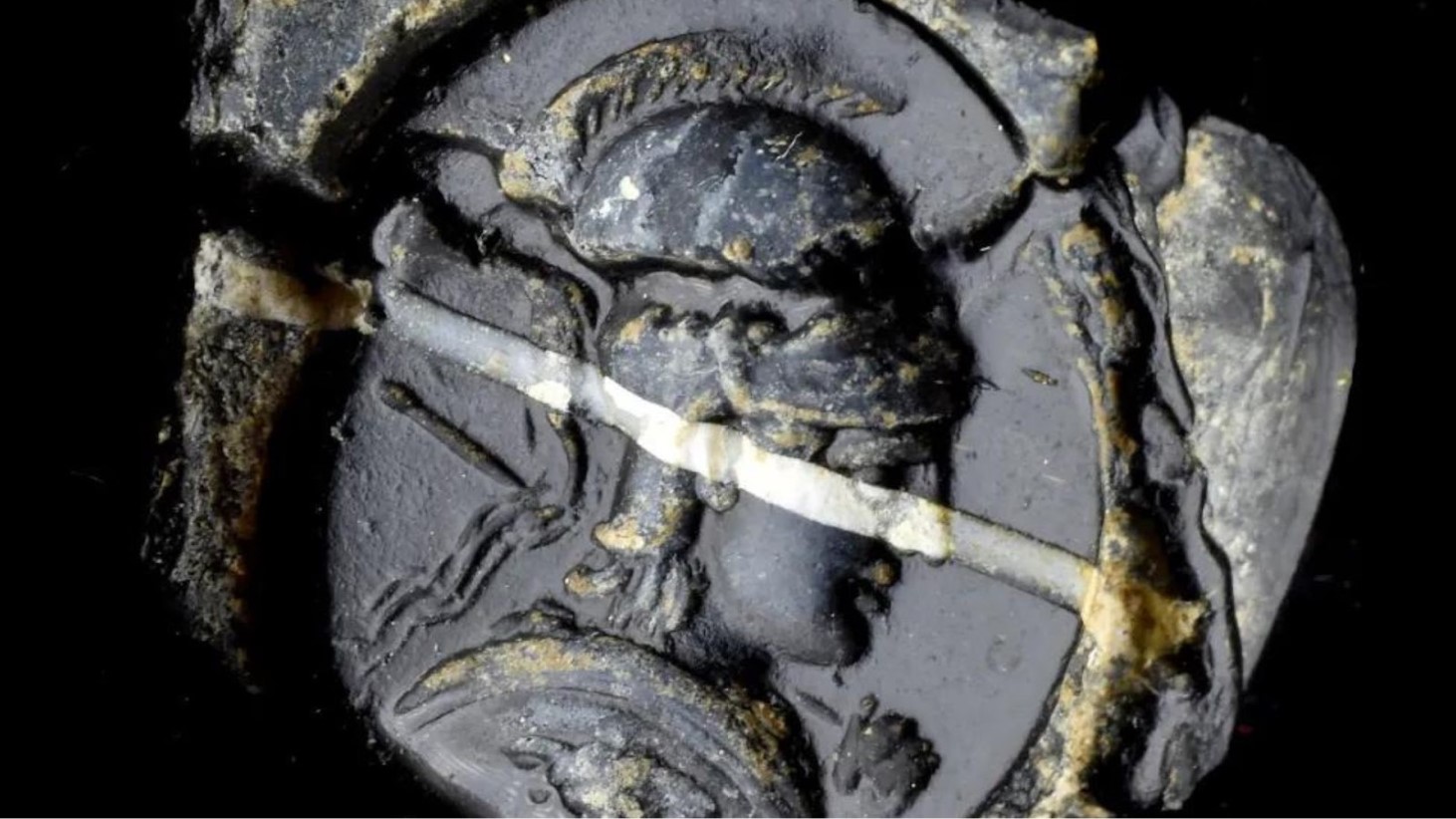 Close-up photo of a gray stone sculpture of what appears to be a Roman soldier. They areis wearing a helmet and holding a spear