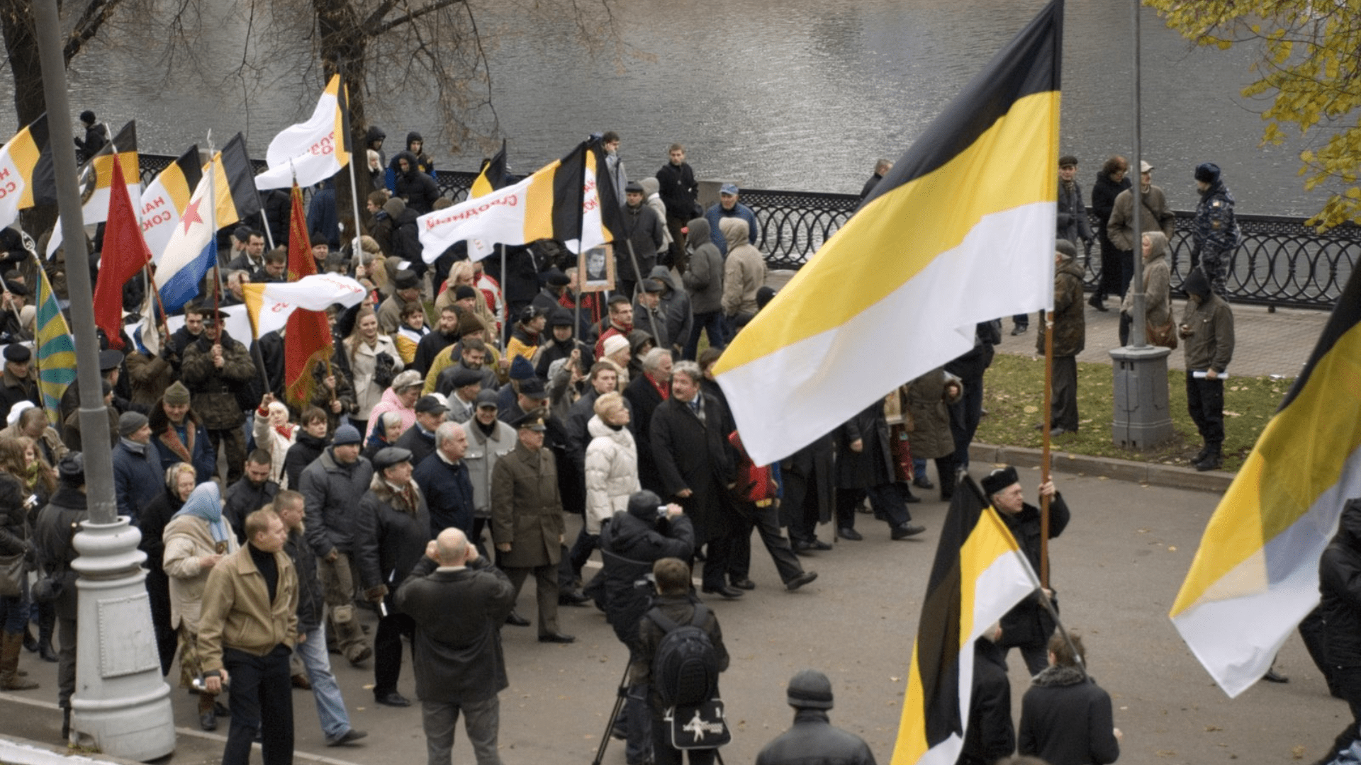 A demonstration of Russian nationalists holding various flags and walking through a city street.