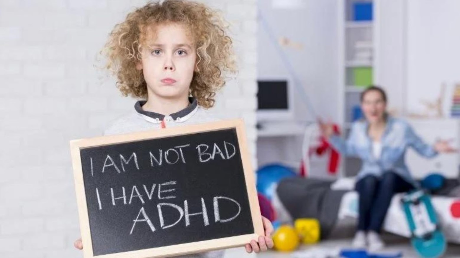 Child holding a sign that reads “I’m not bad, I have ADHD” in front of a stressed out mother