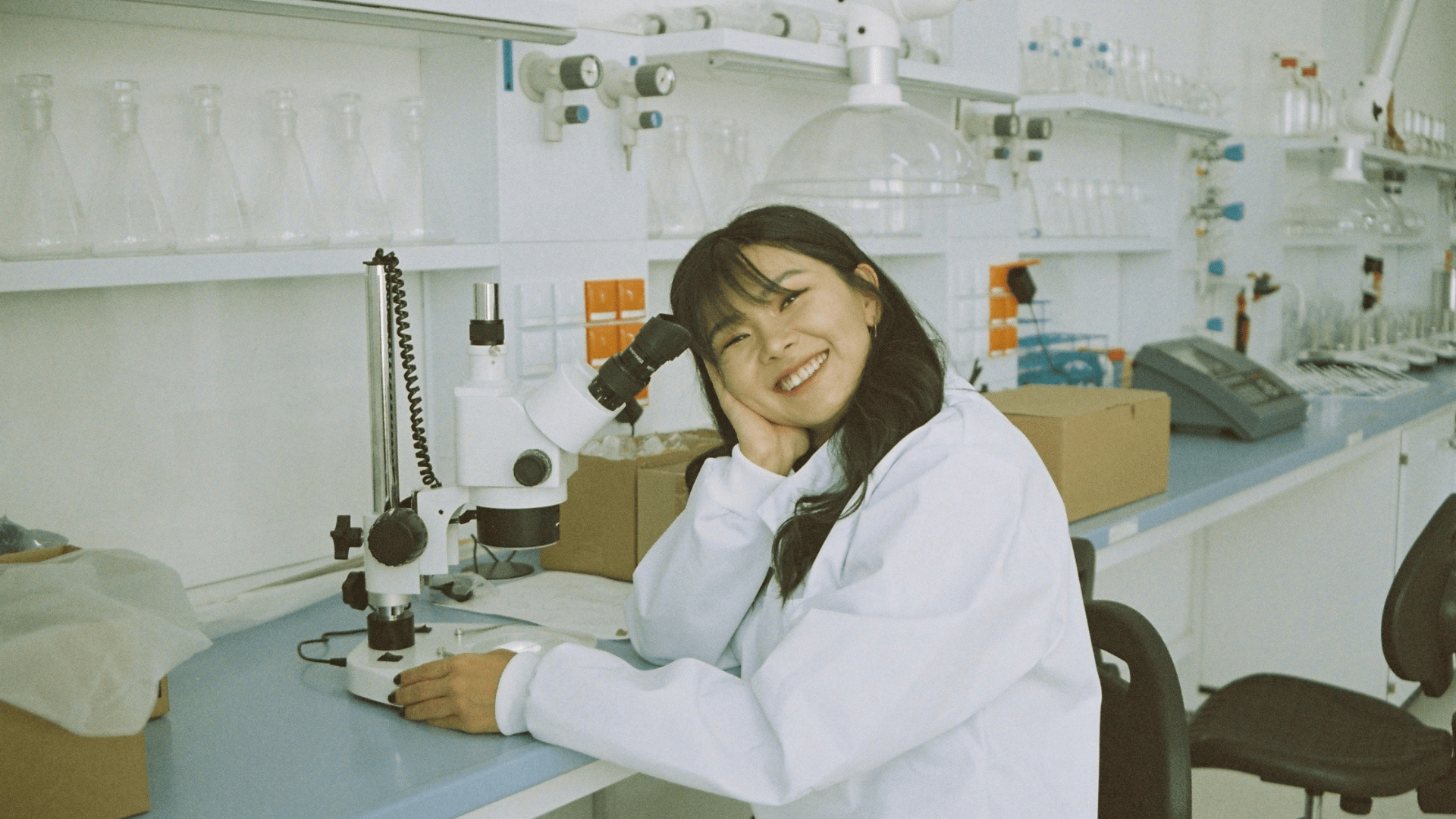 A smiling scientist sitting at the research bench in front of a microscope.