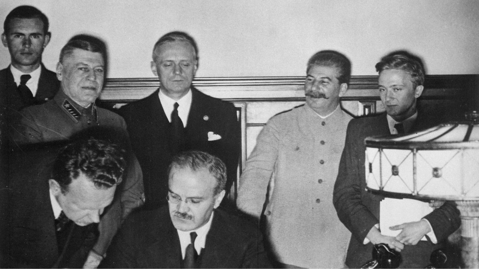 A black and white photo of a group of men, including Joseph Stalin, during the signing of the Molotov-Ribbentrop Pact.