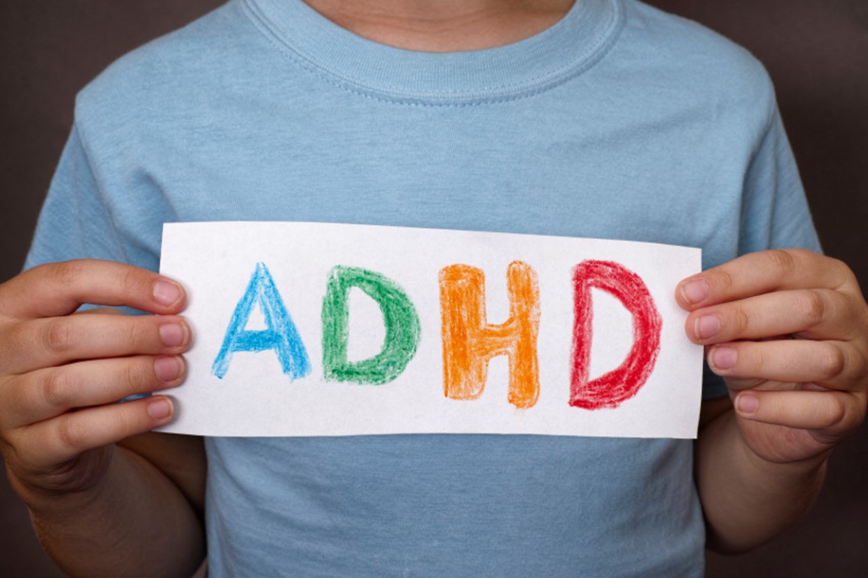 Faceless child holding a hand-made sign that reads “ADHD”