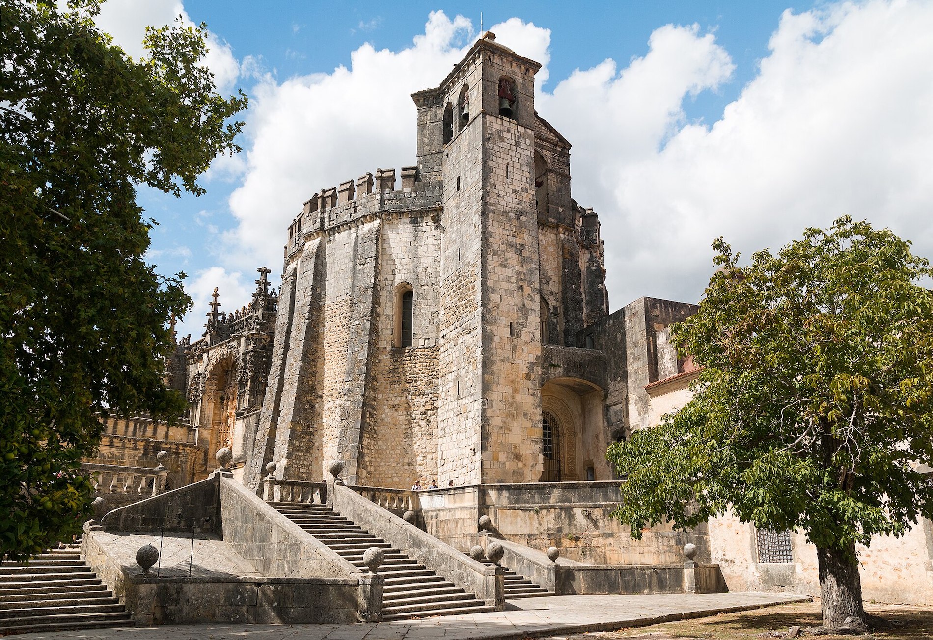 A large stone castle in surrounded by trees with a blue sky in the background