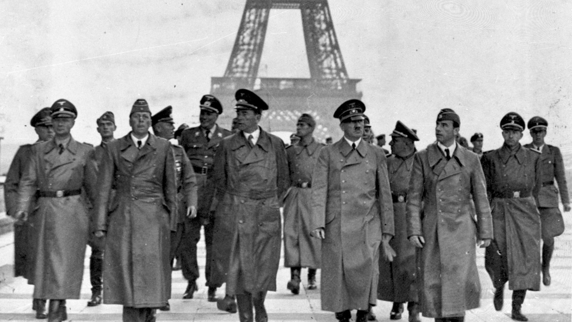 A black and white photo of Adolf Hitler and other Nazi German officers walking in front of the Eiffel Tower in Paris in 1940