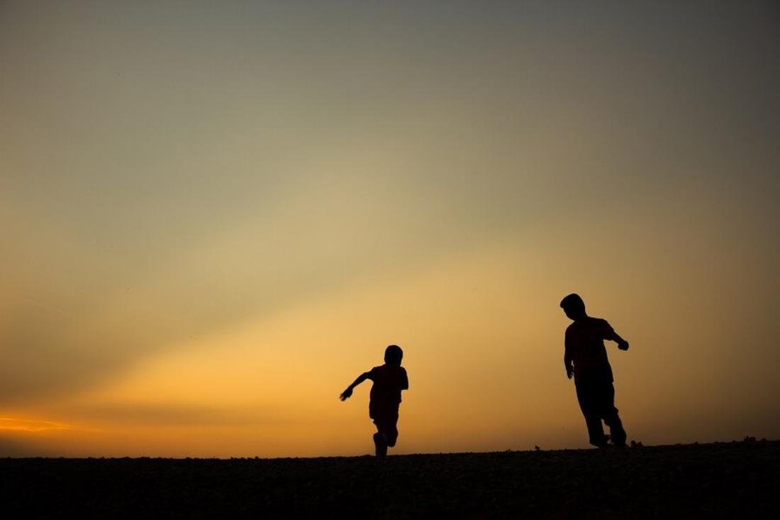 Silhouette of an adult man and a young boy playing at sunset