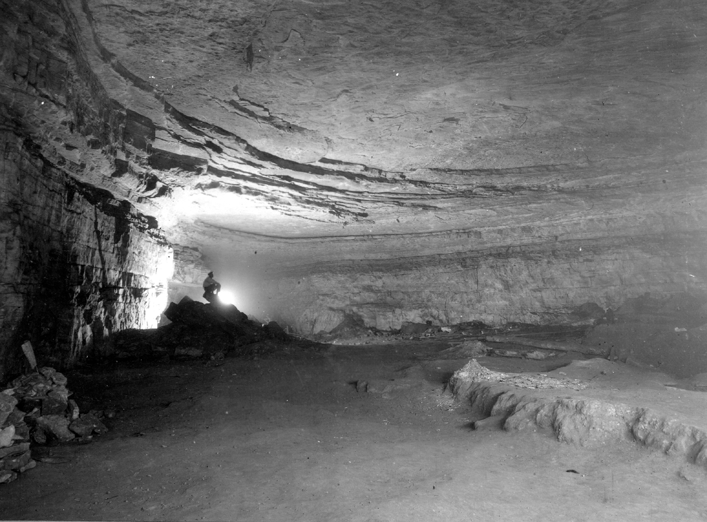 Black-and-white photo of Mammoth Cave's Rotunda Room. A spelunker sits at the far end of the room with a headlamp on.