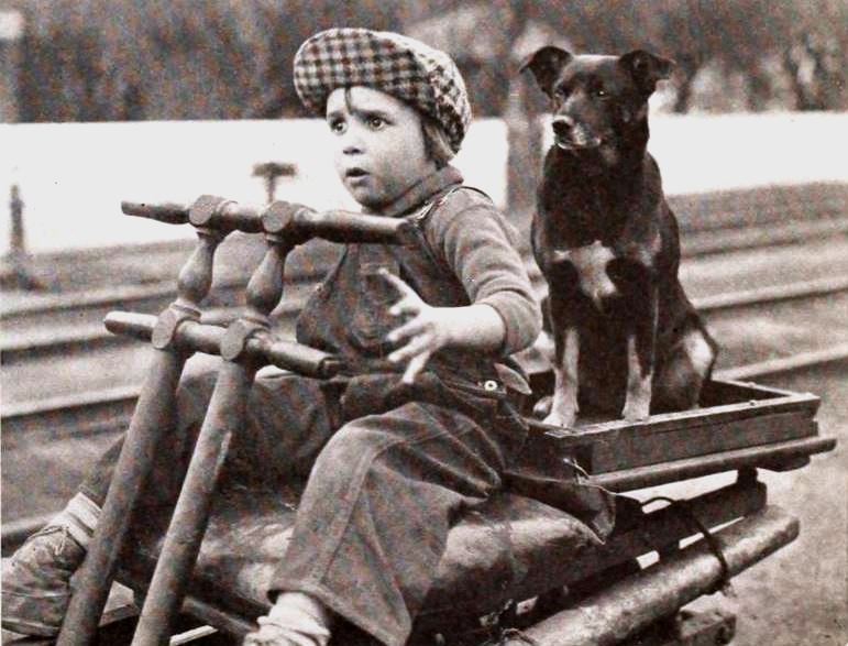 Jackie Coggan riding a wagon with a dog on the back in Peck's Bad Boy (1921).