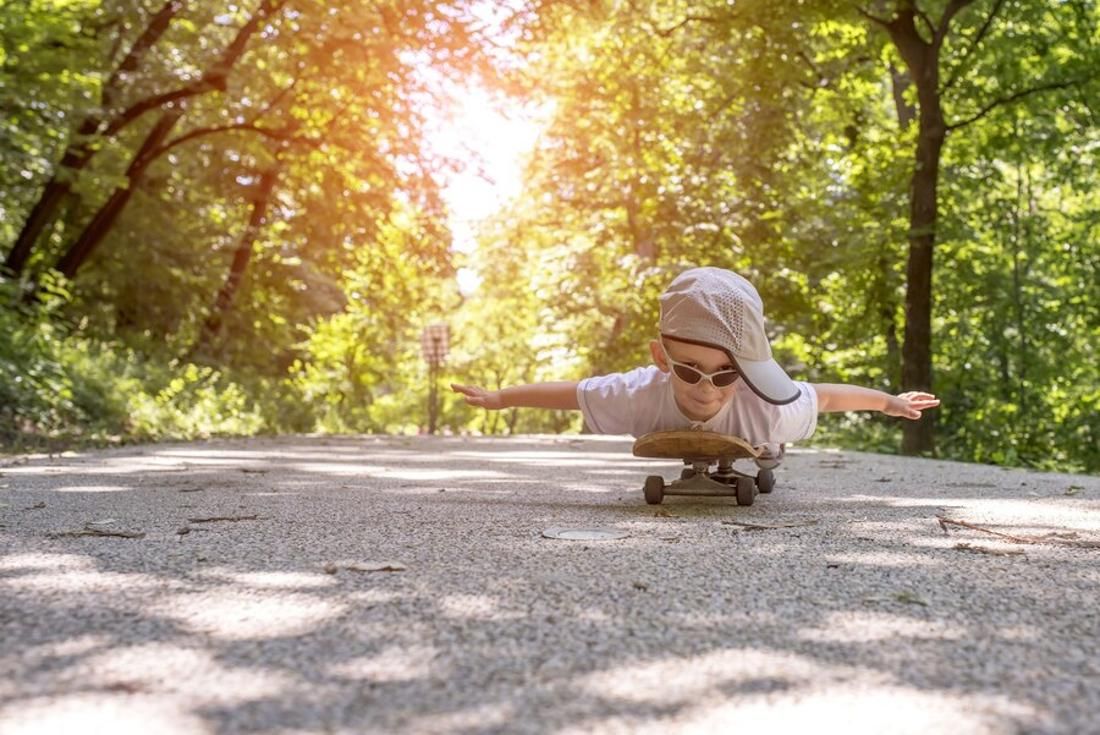 Young boy in a hat and sunglasses plays on a skateboard on a residential street