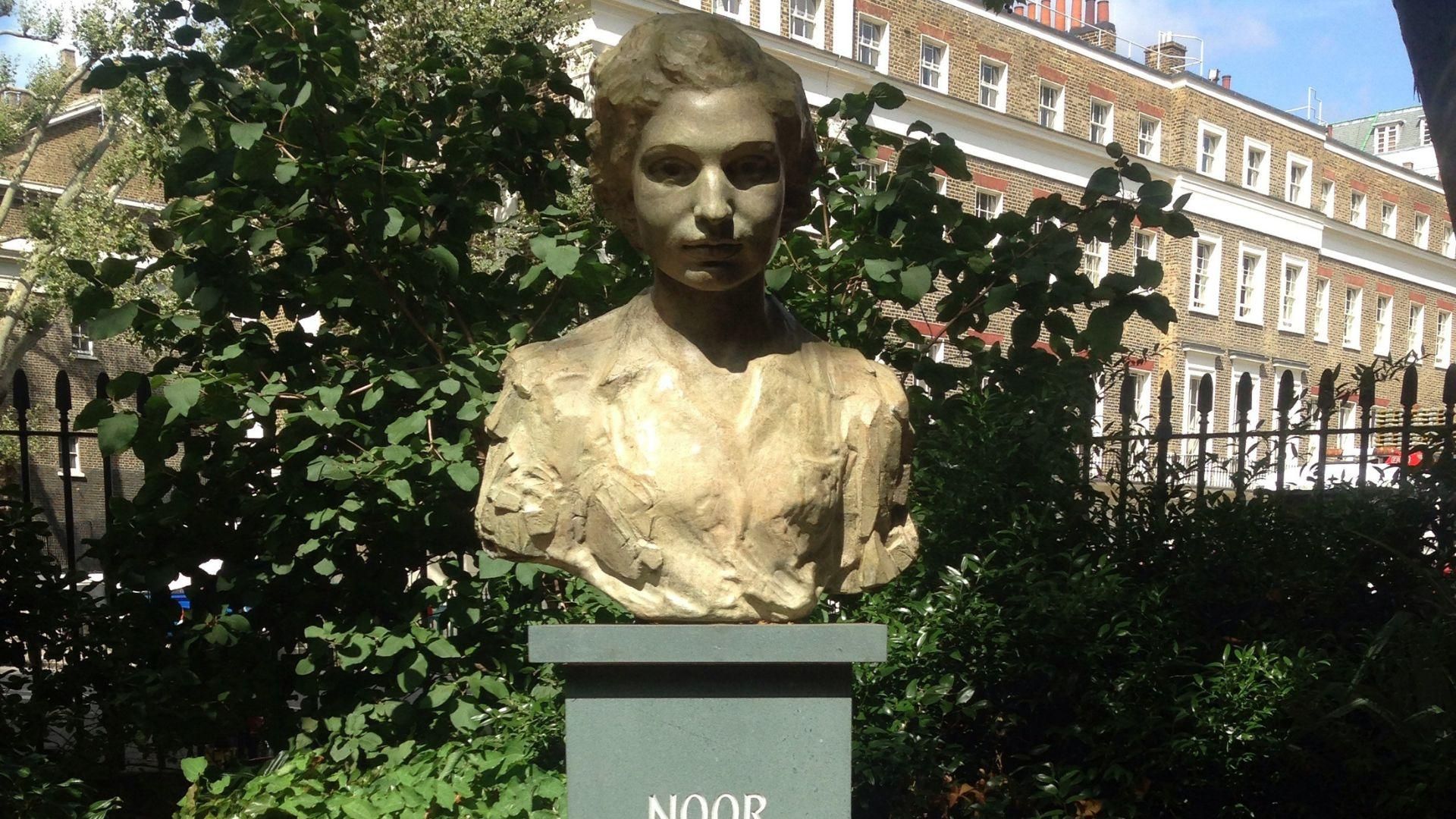 A sculpture of Noor Inayat Khan by bushes and buildings.