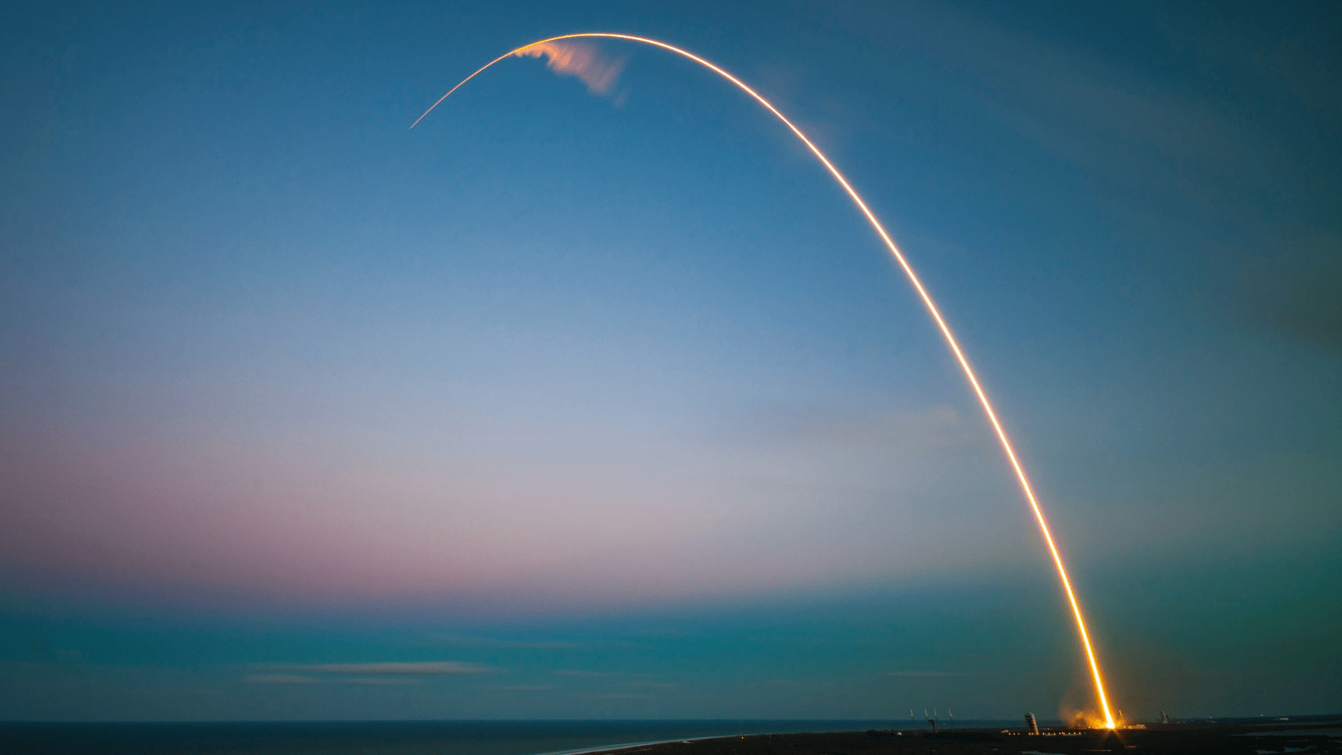 A SpaceX rocket launches from Cape Canaveral, arching far across the sky in a streak of bright light.