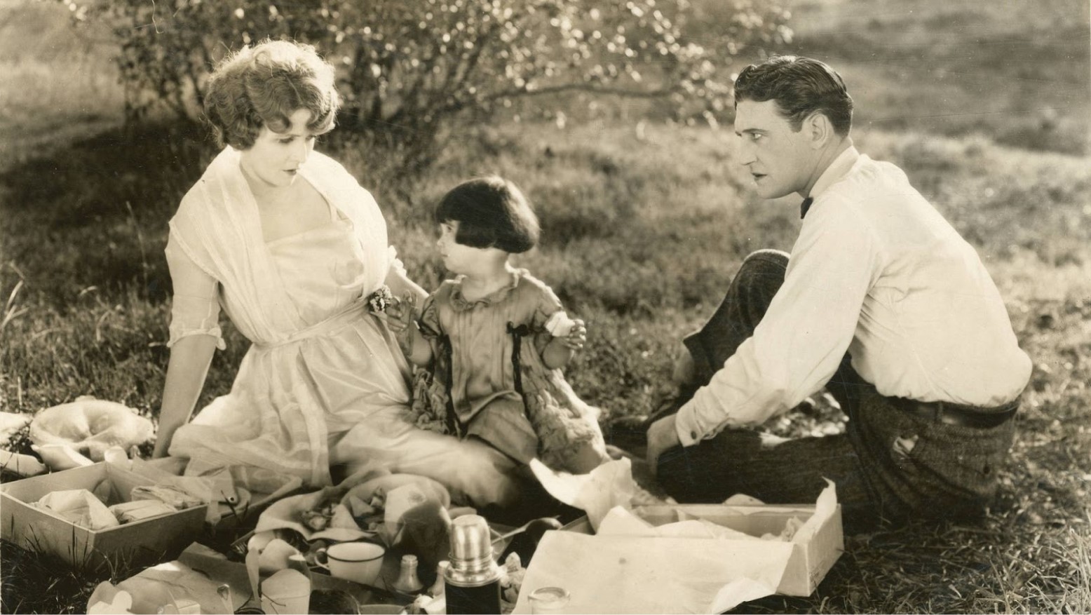 A movie still from the 1922 film “Fools First”, showing Claire Windsor, Diana Serra Cary, and Richard Dix sitting down outside together.