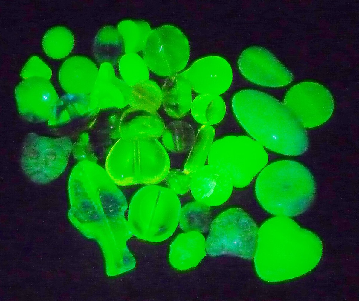 An image of several uranium glass beads under UV lights