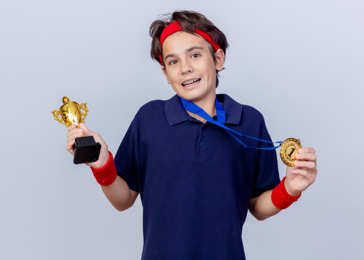 A young kid dressed in a blue polo shirt holds up a small trophy and medal