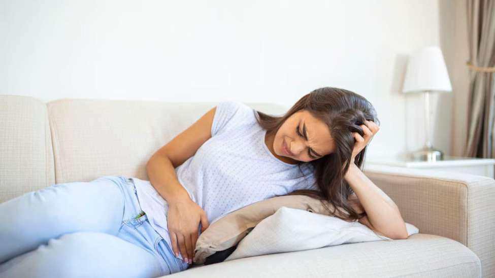Woman laying on the couch while holding her stomach in pain