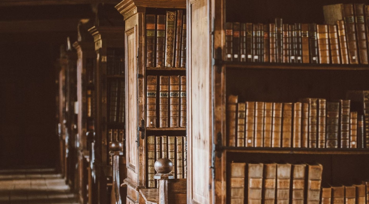 An old library. There are various old, brown, wooden bookshelves that all have old books on each shelf.