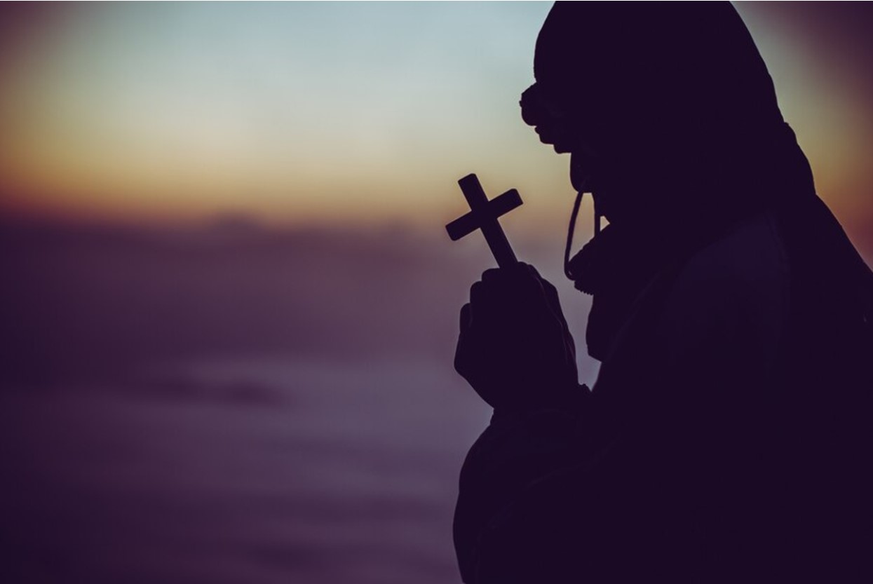 Silhouette of a man holding a cross while praying