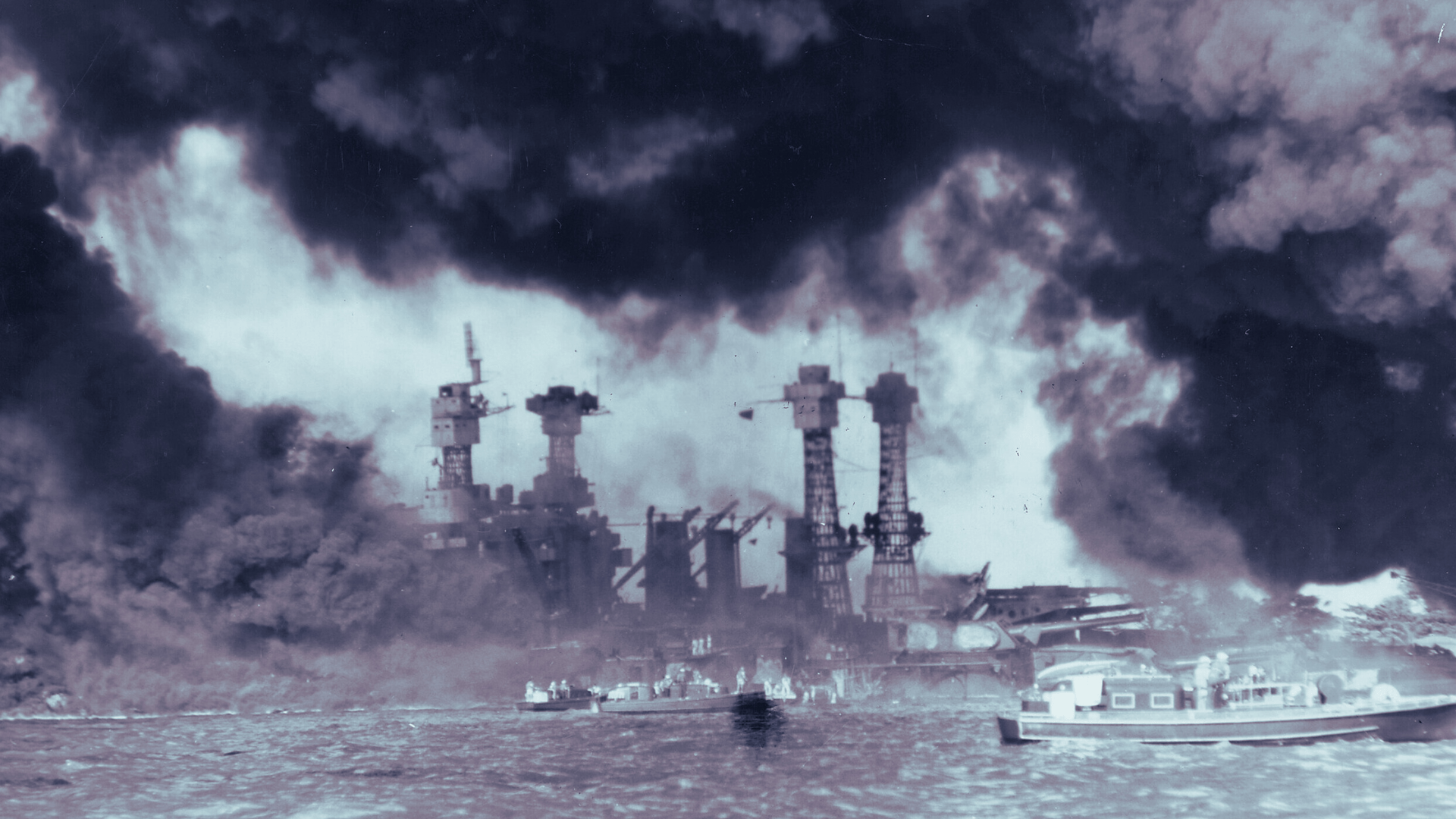 Black-and-white photo during the attack on Pearl Harbor. Black smoke billows into the air as small boats move along the water. Structure can be seen across the water between rolling clouds of smoke.