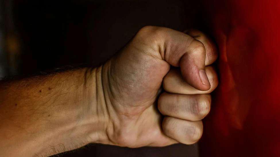 Someone punching a wall. Their fist is clenched and the wall is red, with a dent from the punch in it.