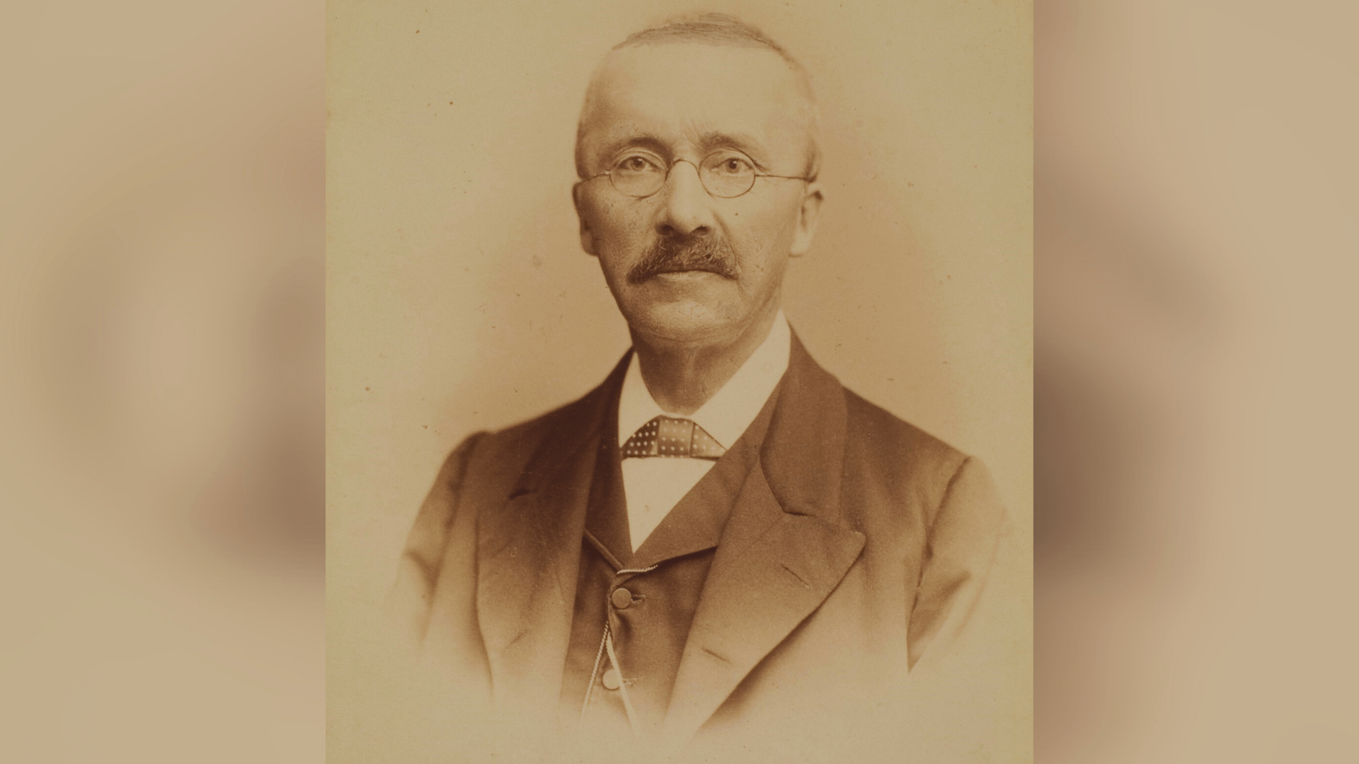 A black-and-white photo portrait of Heinrich Schliemann wearing a suit and glasses.