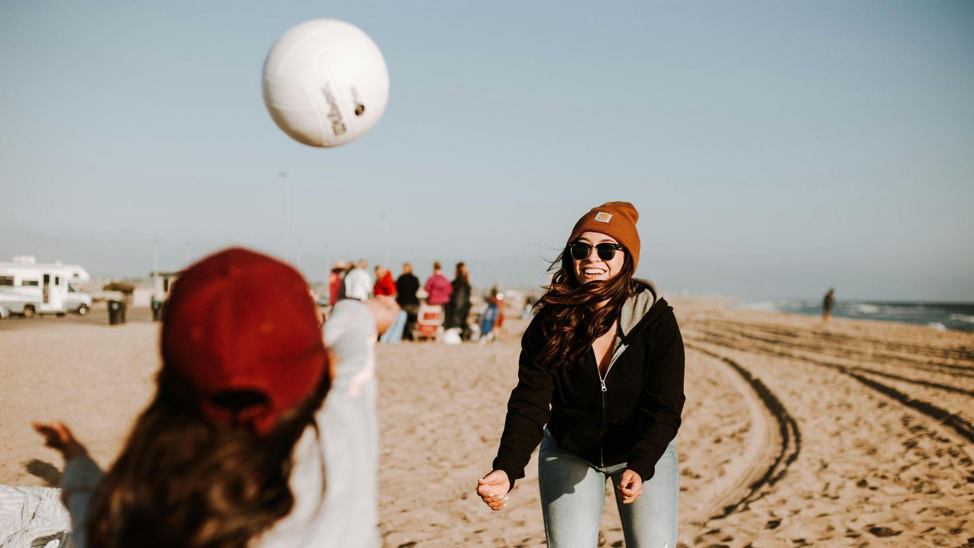 Two girls playing volleyball together at a beach in the daytime.