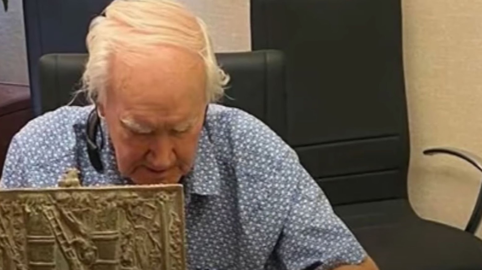 Forest Fenn wearing a blue shirt with his gold treasure chest in front of him. He is looking down at the contents inside it.