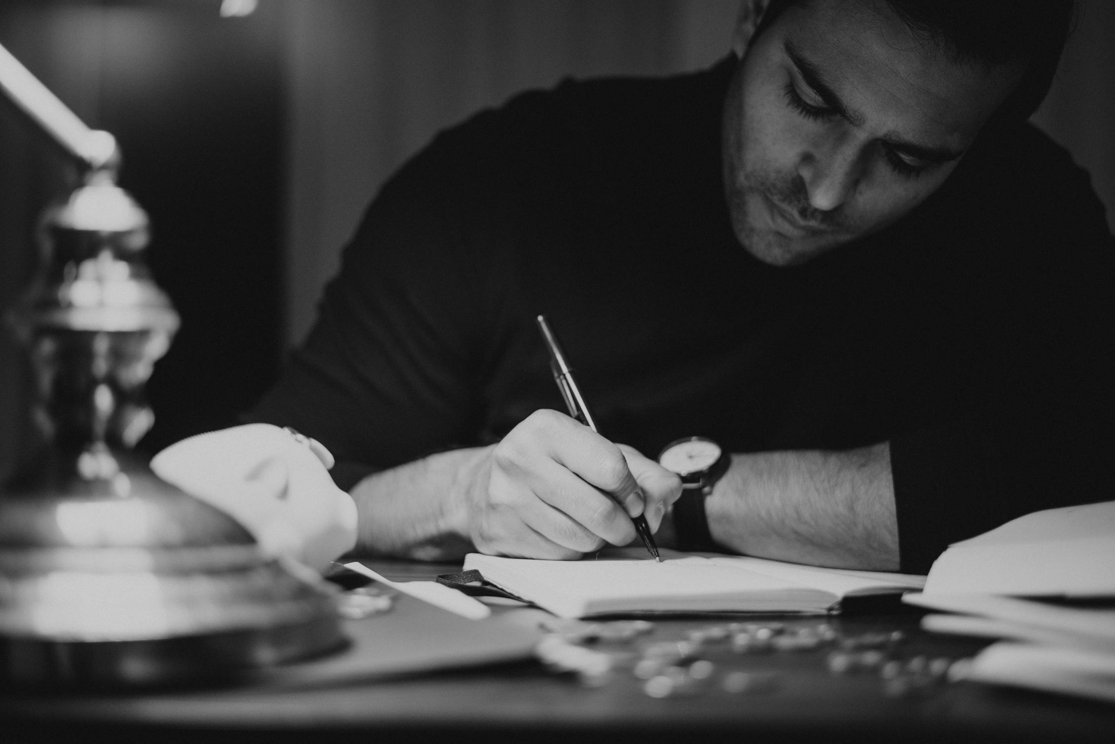 Crop man taking notes in copybook in dark home office