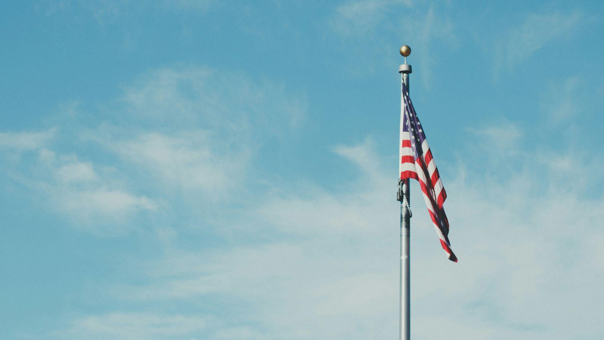 An American flag on a pole against a cloudy blue sky.