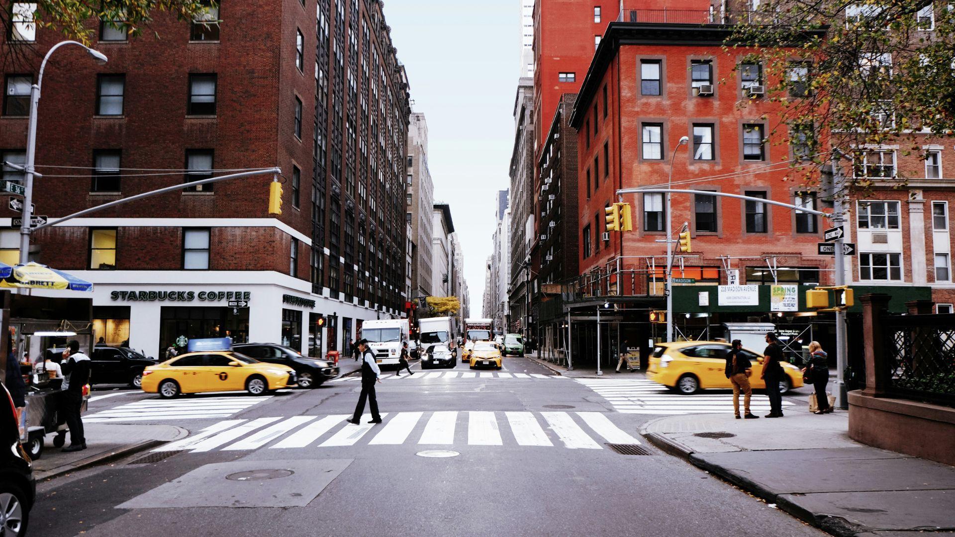 People walking down the street and sidewalks as cars drive past in New York.