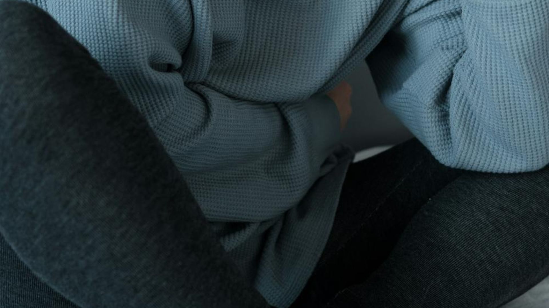 A person wearing a green wool jumper and linen trousers.
