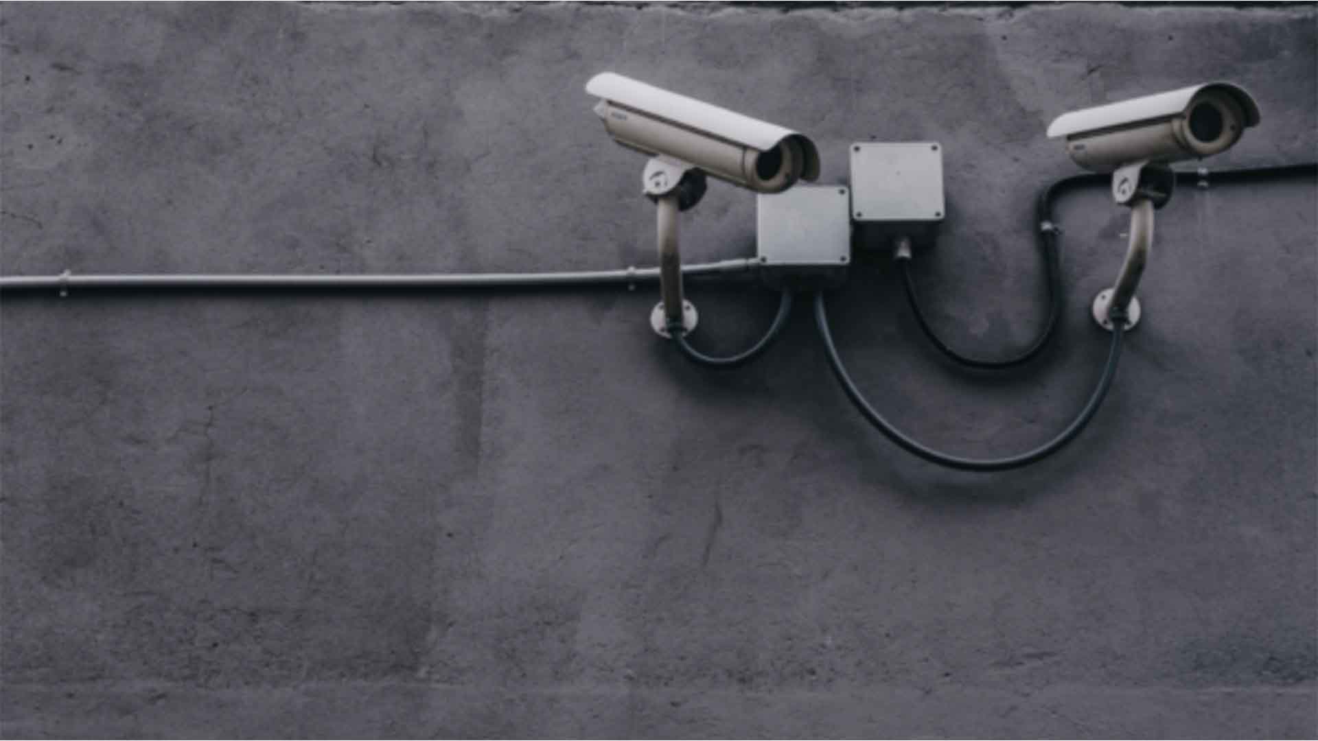 Two security cameras against a wall.