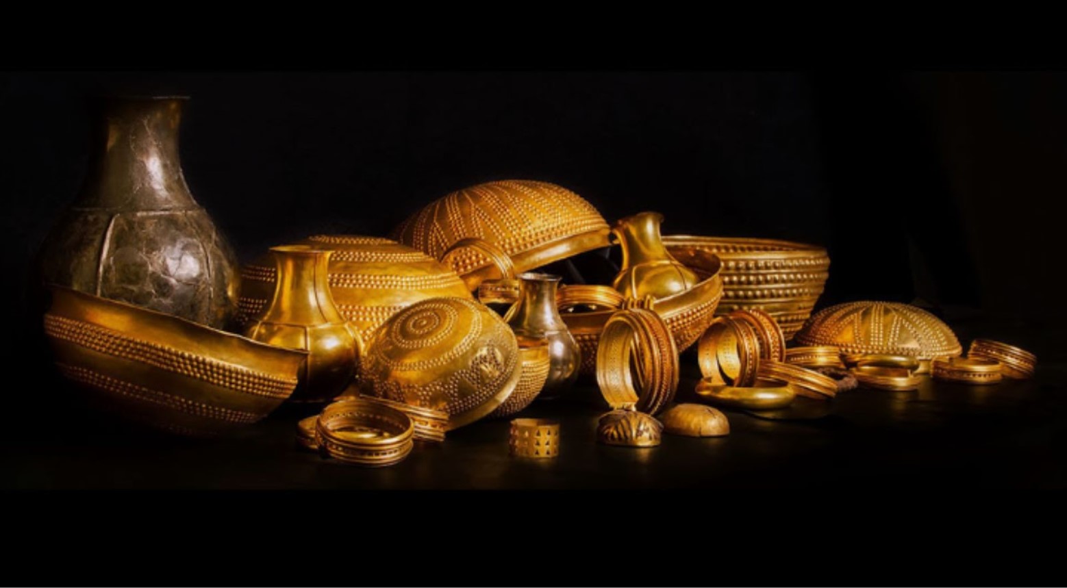 The Treasure of Villena against a black background. There are gold bowls, vases, and bracelets as part of the collection.
