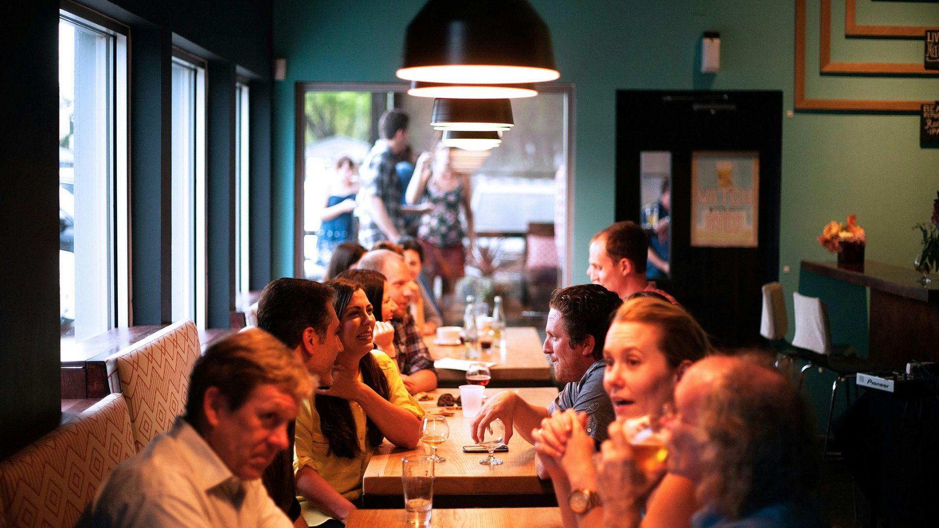 Many people sitting down at tables and talking to each other.