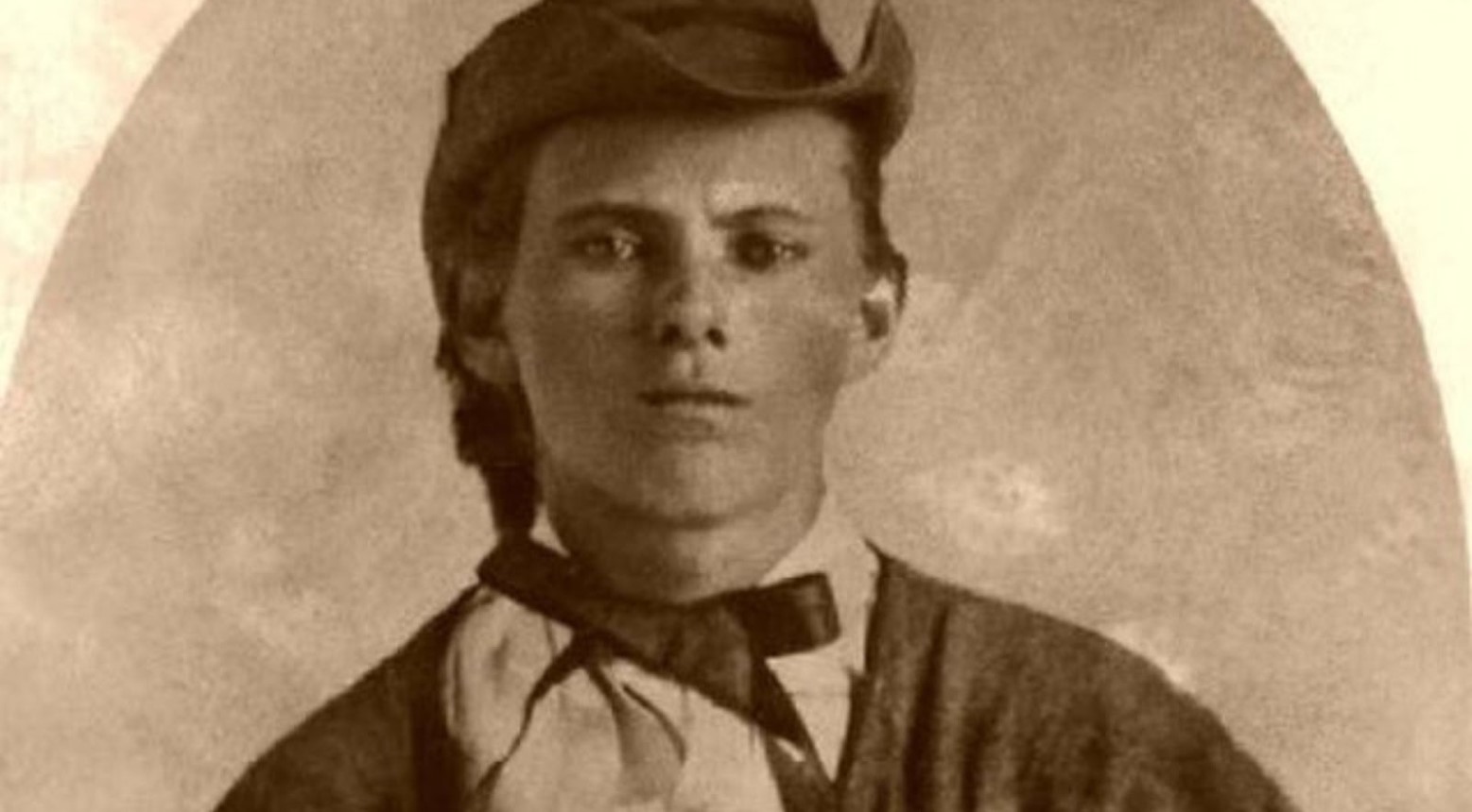 A black and white photo of Jesse James wearing a hat and a shirt with a bow on.