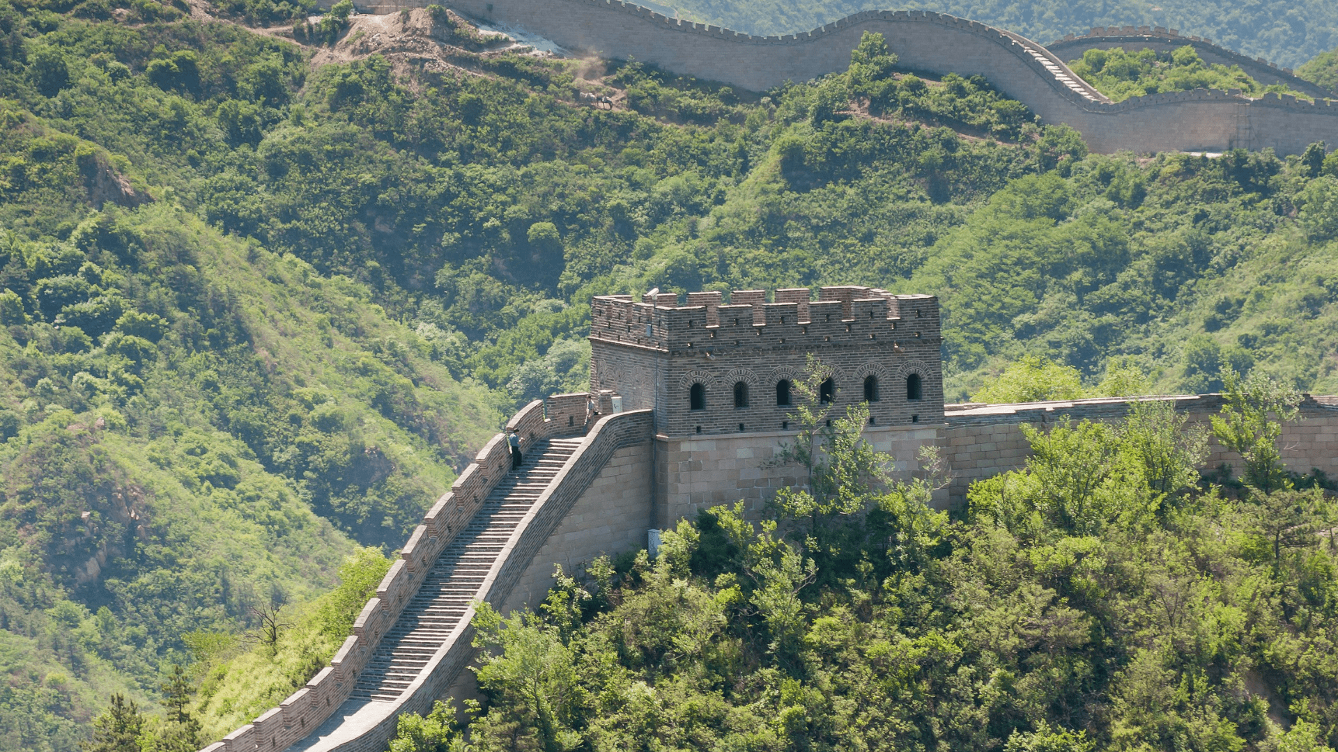 A portion of the Great Wall of China in Badaling, China. Rolling green hills surround the wall.