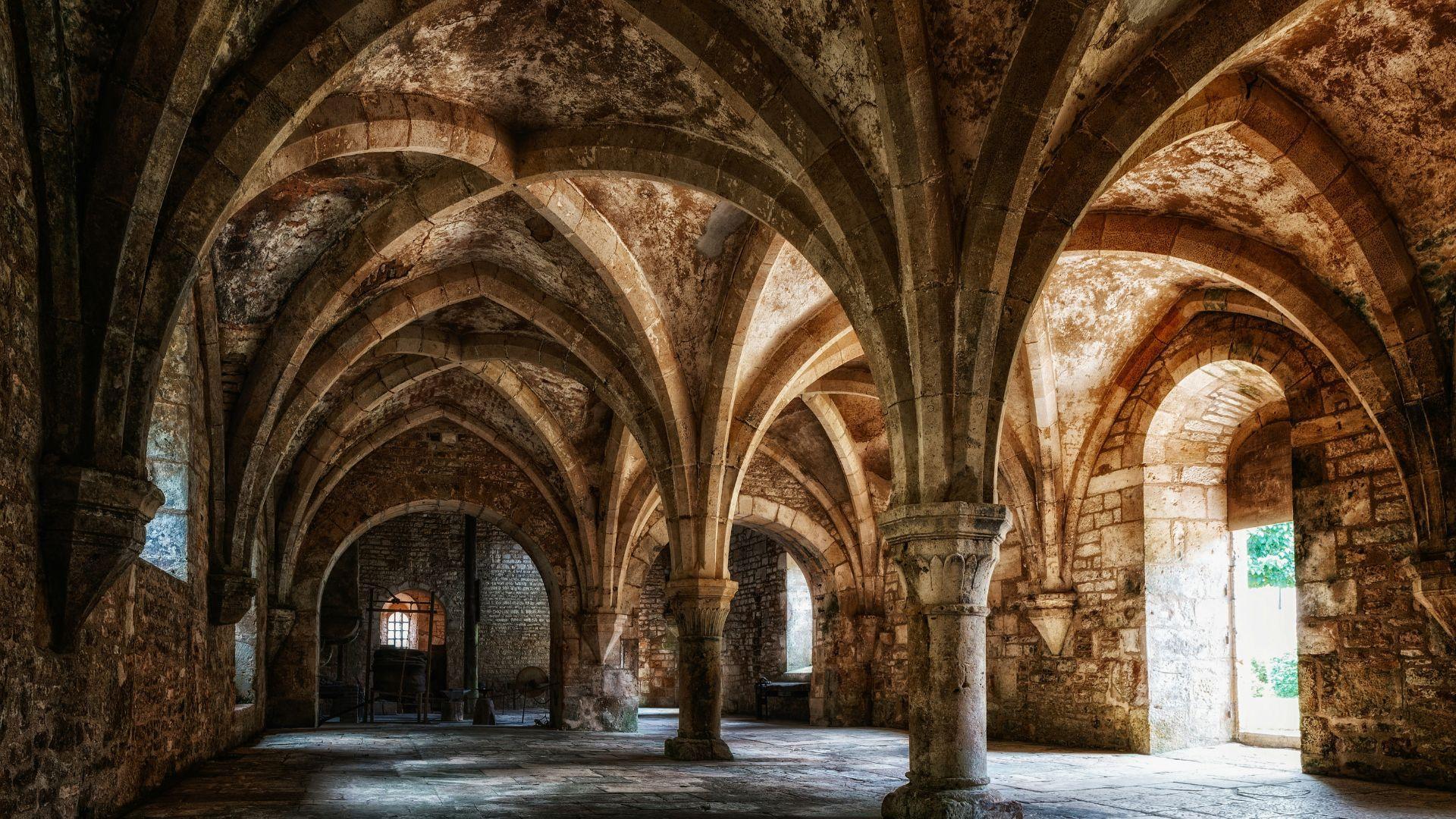 The inside of an old abbey, with stone flooring and high arches, in France.