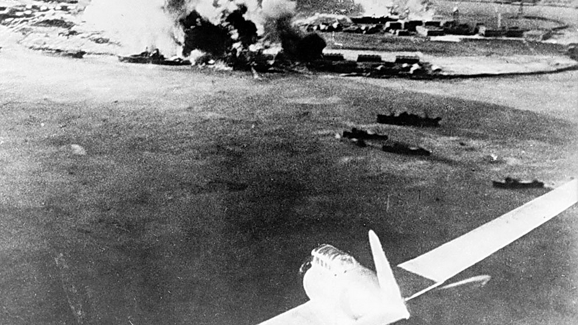 Black-and-white photo of a Japanese plane (presumably an Aichi D3A) attacking Pearl Harbor, Oahu, US Territory of Hawaii, on 7 Dec 1941.