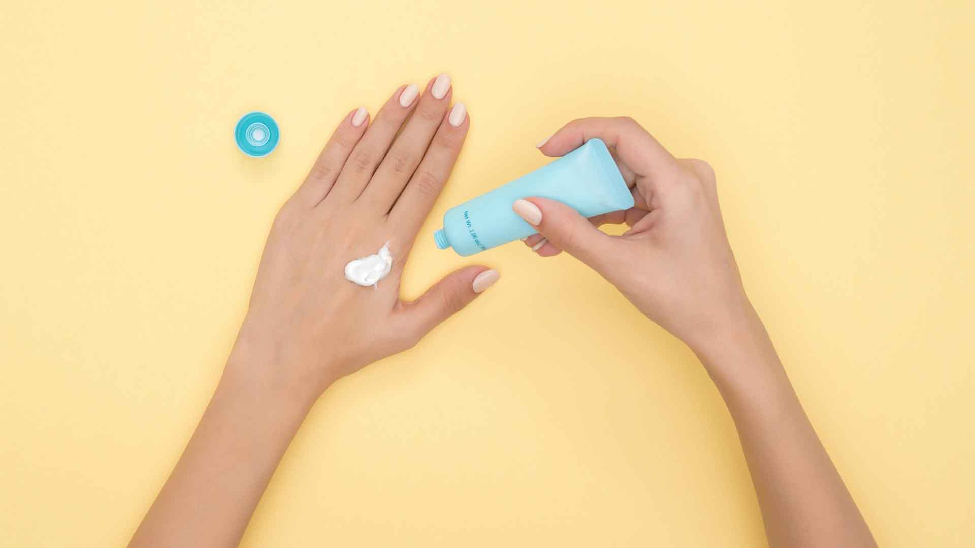 Person pouring plastic tube bottle of skin cream