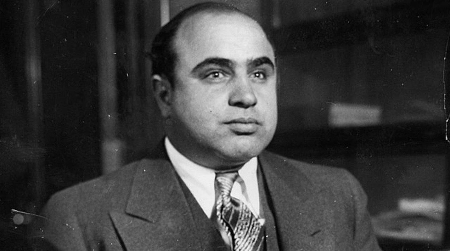 A black and white photo of Al Capone. He is wearing a suit and has a neutral expression whilst looking off to the side of the camera.